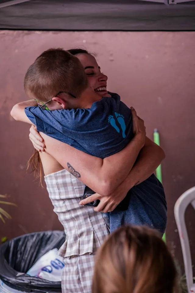 Duas pessoas se abraçam, sorrindo, durante um encontro de ação social