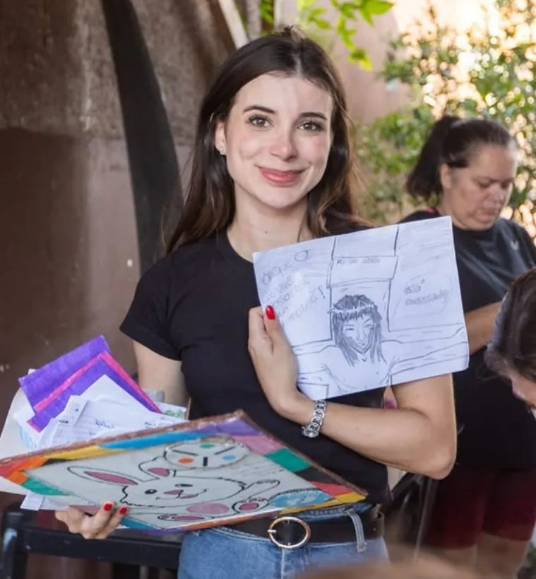 Bárbara Maria Vieira sorri segurando desenhos coloridos em uma atividade de projeto social