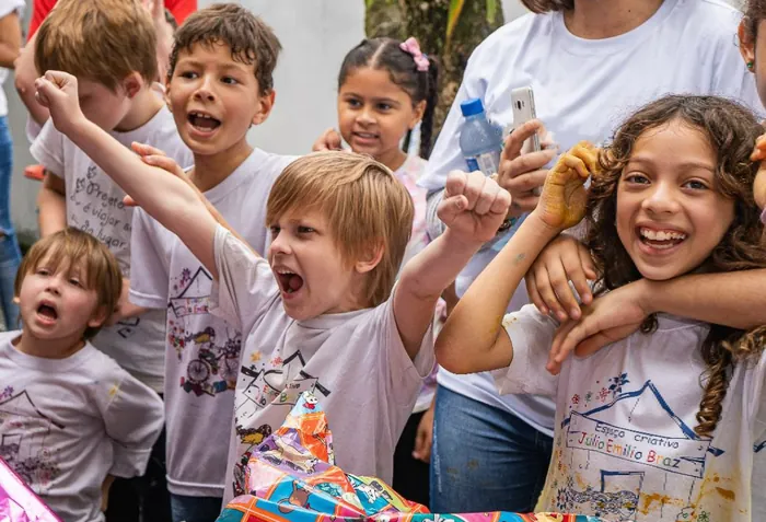 Crianças comemorando com os braços erguidos durante atividade de projeto social
